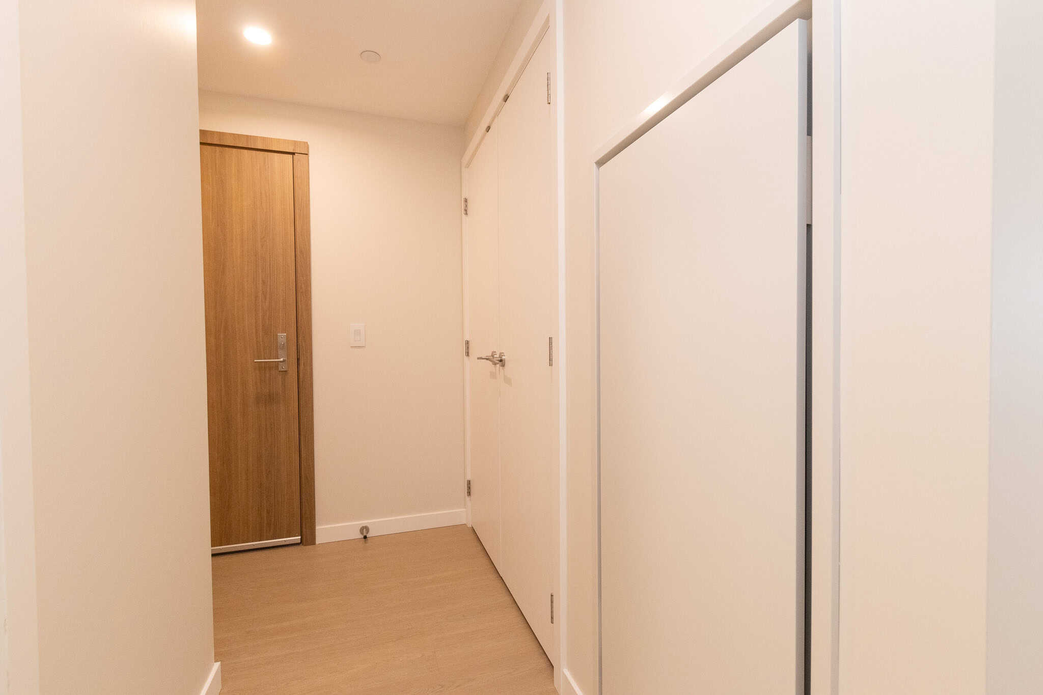 Bright modern hallway interior with white walls, wooden door, and built-in closet, showcasing contemporary condo features offered by Orca Realty Inc.
