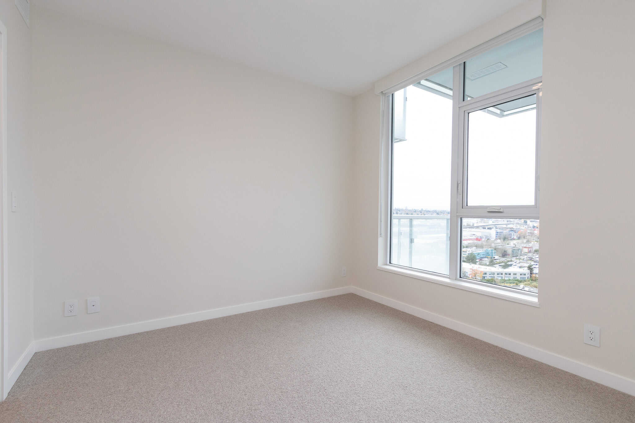 Spacious modern apartment bedroom with large window and city view, bright and airy, featuring neutral colours, ideal for Vancouver real estate and property rental in BC.