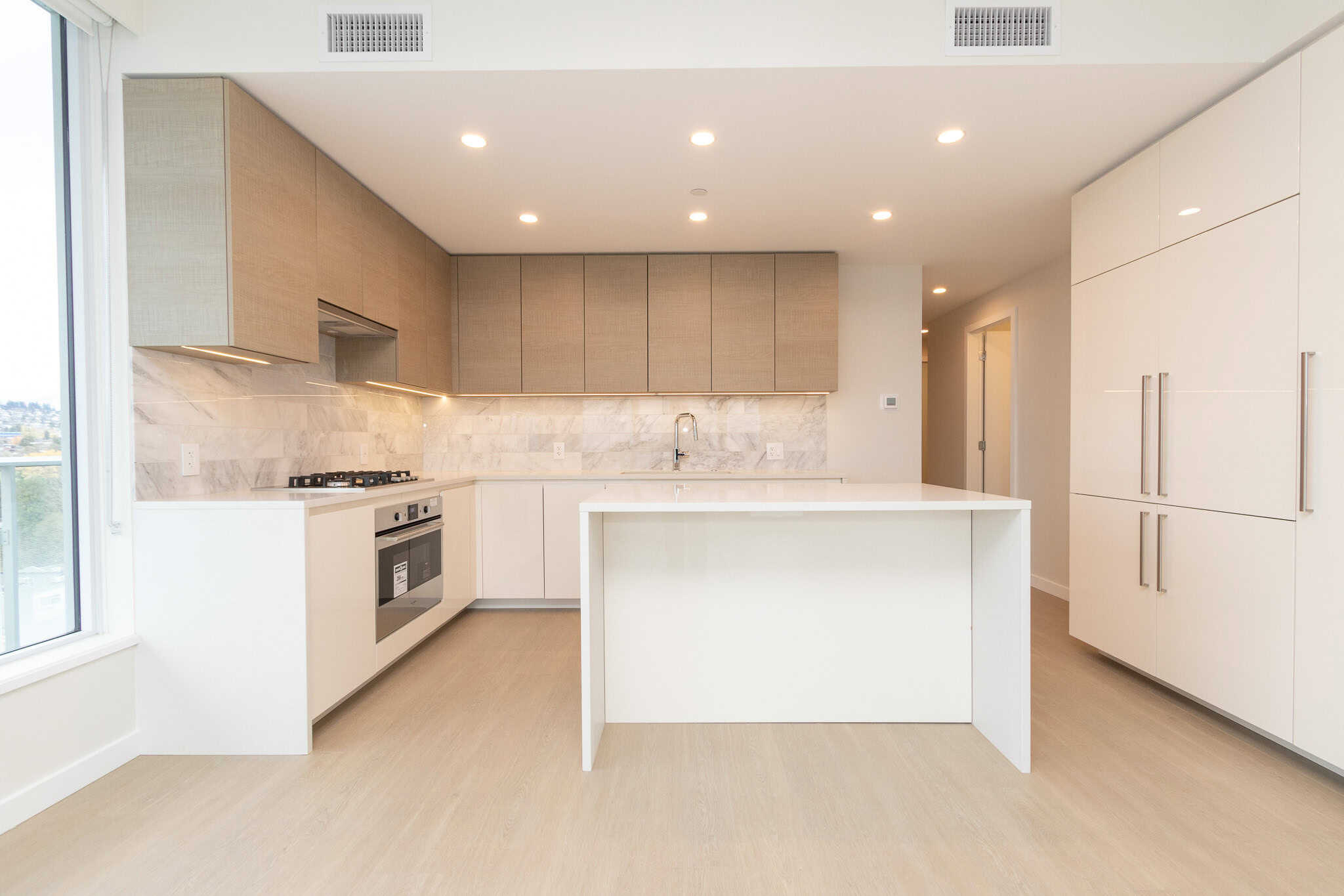 Modern minimalist kitchen with white cabinetry, marble backsplash, and island, showcasing upscale Vancouver real estate from Orca Realty Inc. in a bright, open-concept home.