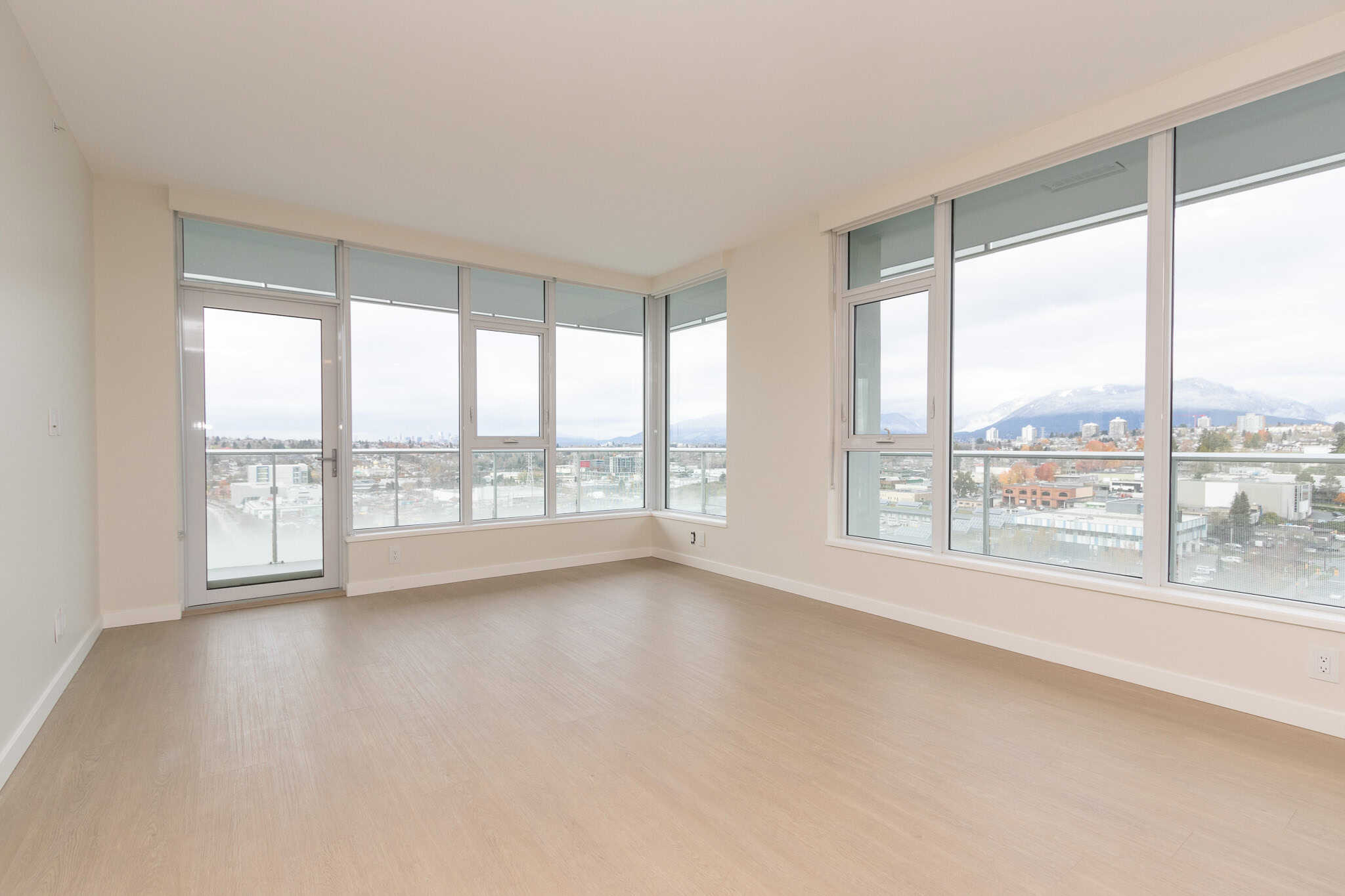 Bright unfurnished condo living room with large floor-to-ceiling windows showcasing city and mountain views in Vancouver, BC. Modern, spacious interior perfect for homebuyers or renters.