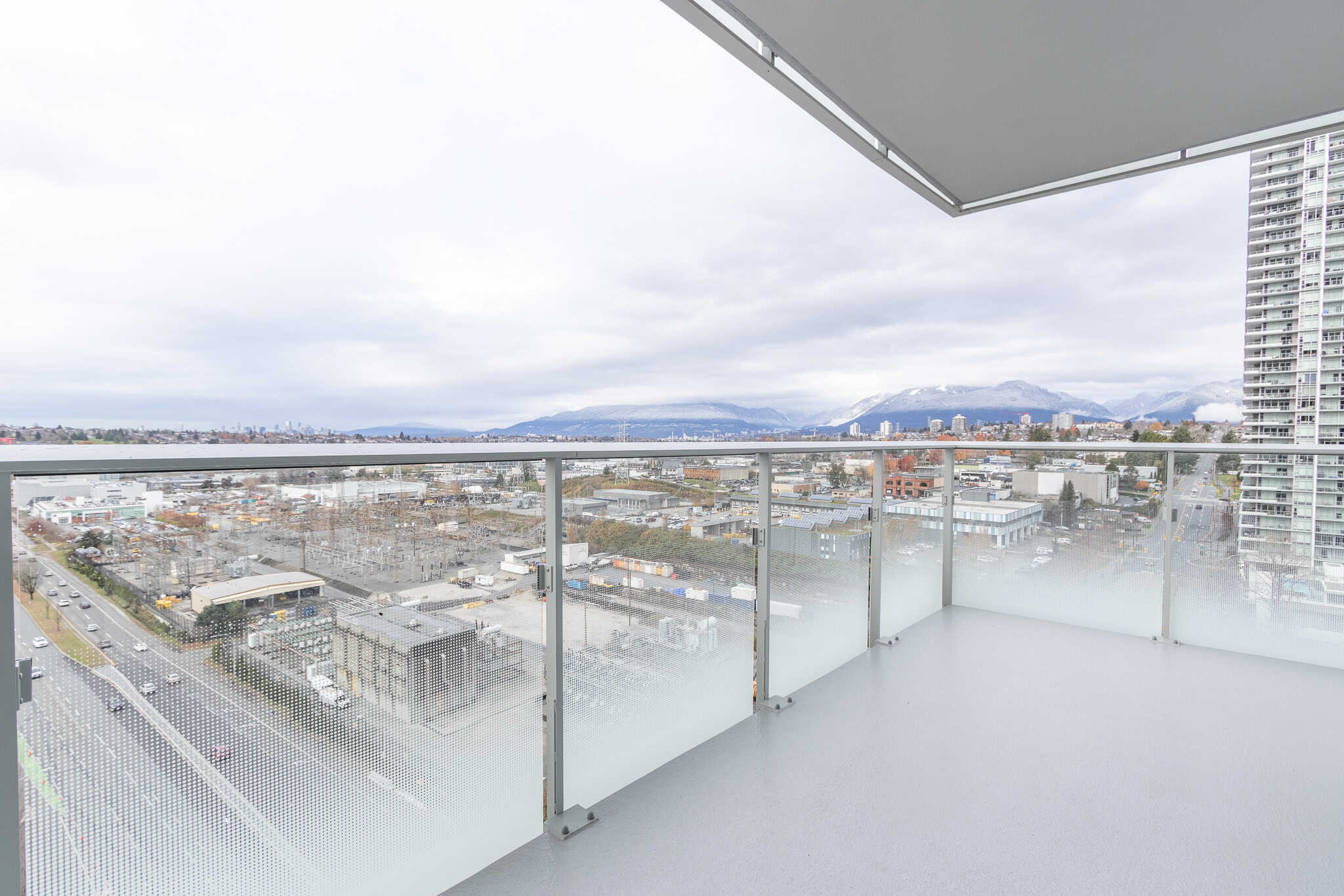 Panoramic view from a modern condo balcony overlooking the city, mountains, and waterfront, emphasizing Vancouver real estate, luxury living, and scenic urban views.