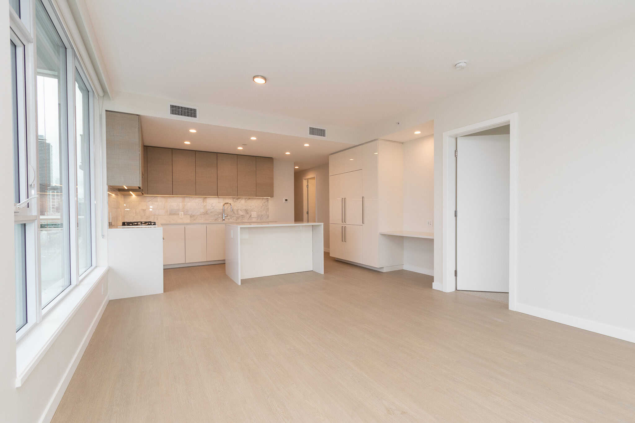 Bright, modern open-concept kitchen with large windows, sleek white cabinetry, marble backsplash, and spacious living area, perfect for Vancouver real estate buyers seeking contemporary homes.