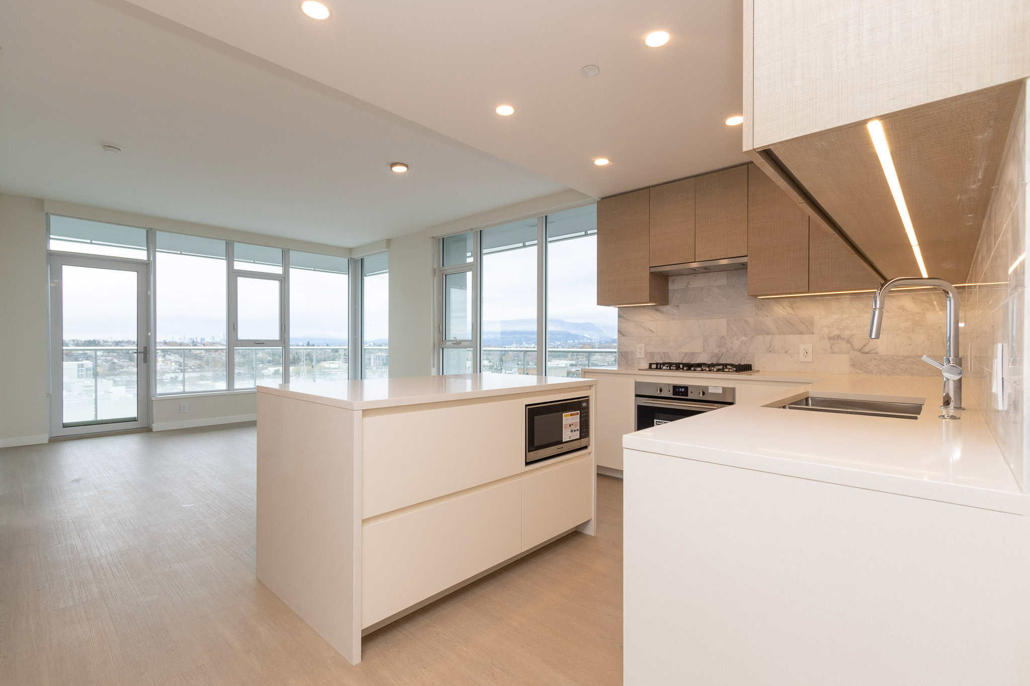 Modern open-concept kitchen with large windows showcasing city views, featuring sleek white cabinetry, built-in appliances, and minimalist design, ideal for contemporary urban living in Vancouver.