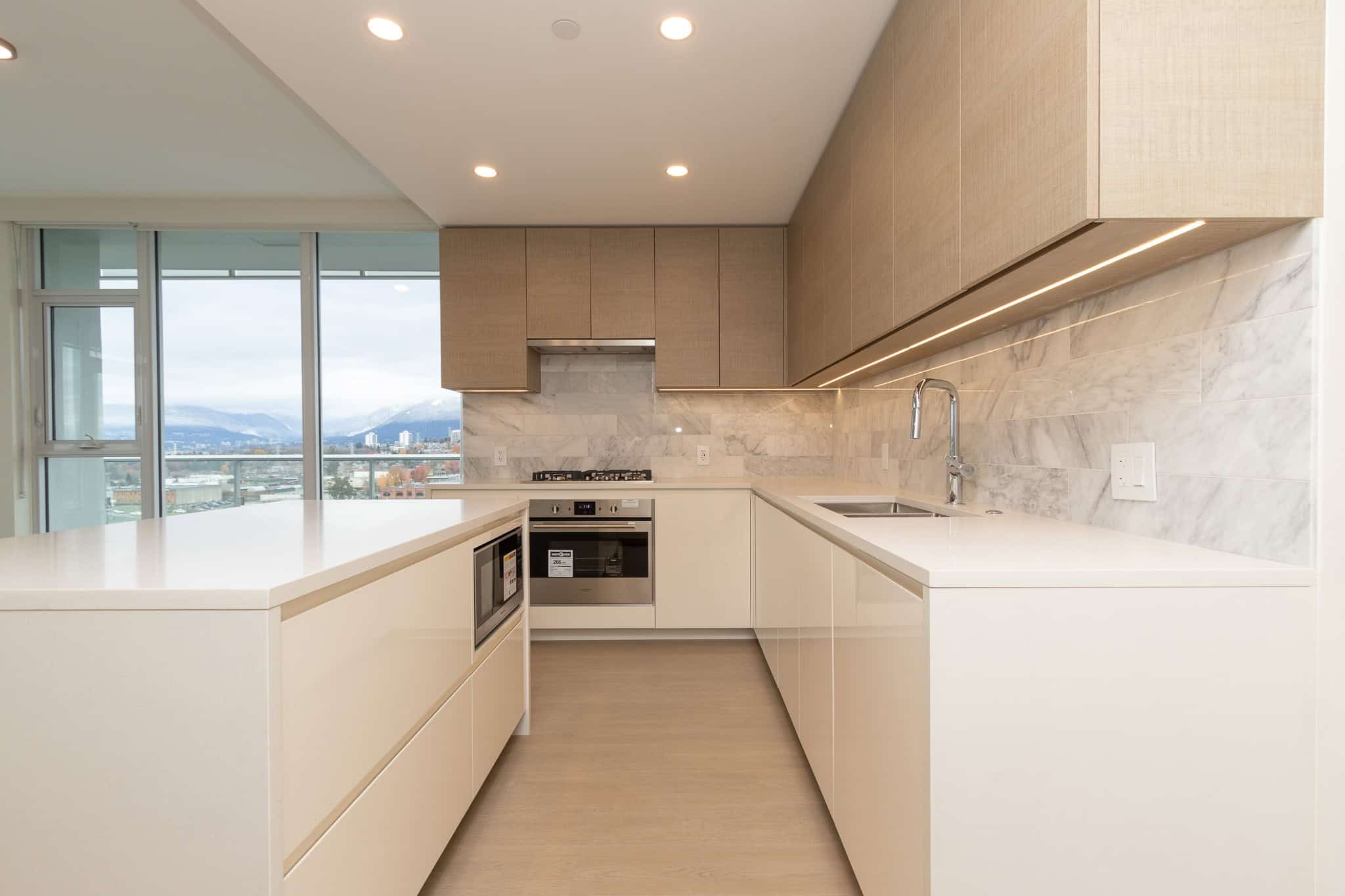 Modern minimalist kitchen with neutral tones, granite countertops, and city view in Vancouver, BC, showcasing contemporary home design by Orca Realty Inc.