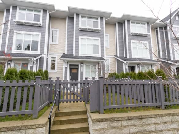 Modern townhouse with grey and beige exterior, featuring large windows, townhouse-style design, and a private front garden with a grey wooden fence, ideal for Vancouver and Lower Mainland real estate.