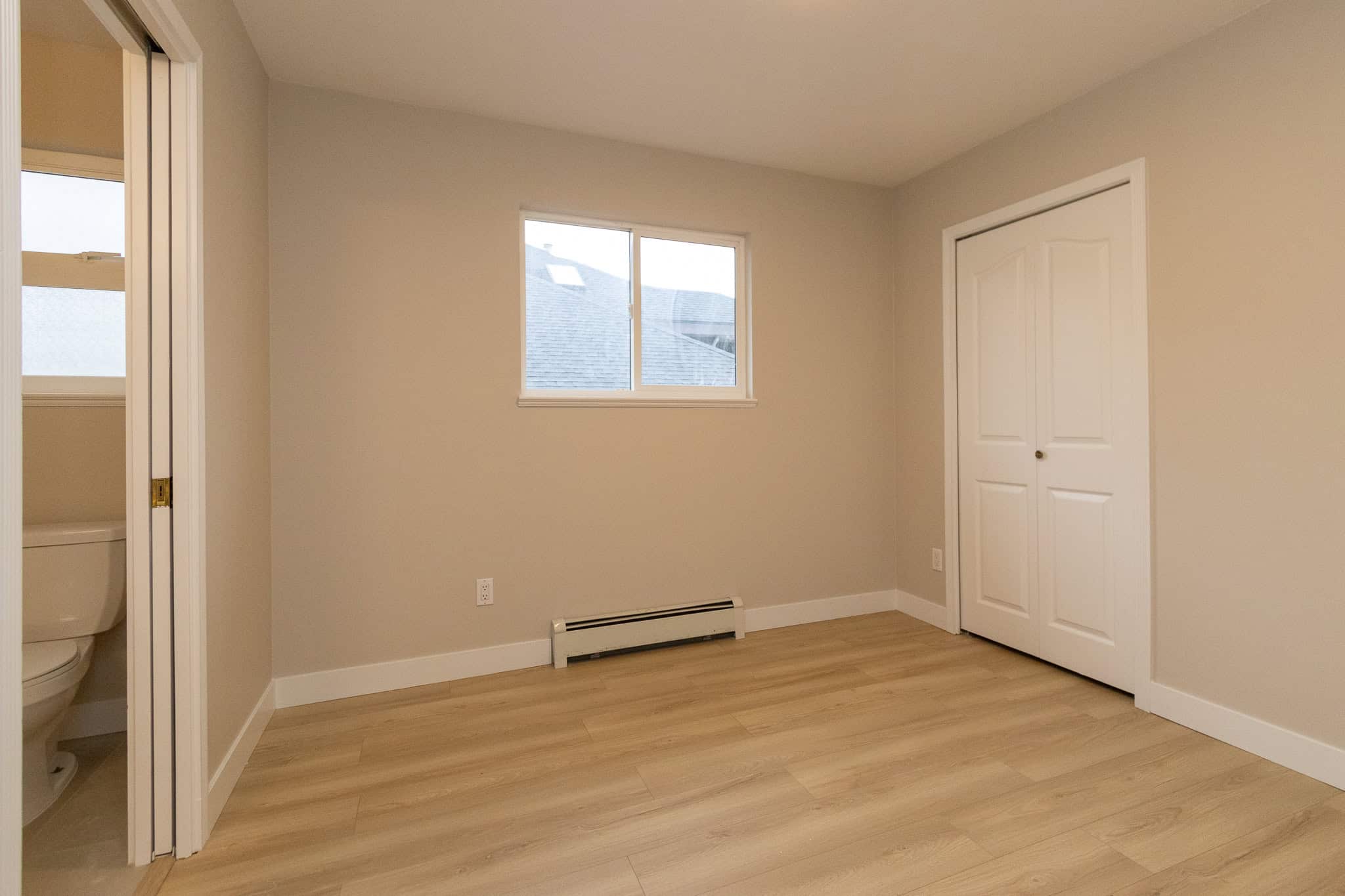 IMG_4350 Spacious bedroom with neutral paint, laminate flooring, and a closet, featuring a window with outdoor views, ideal for Calgary homebuyers seeking cozy and modern interiors.