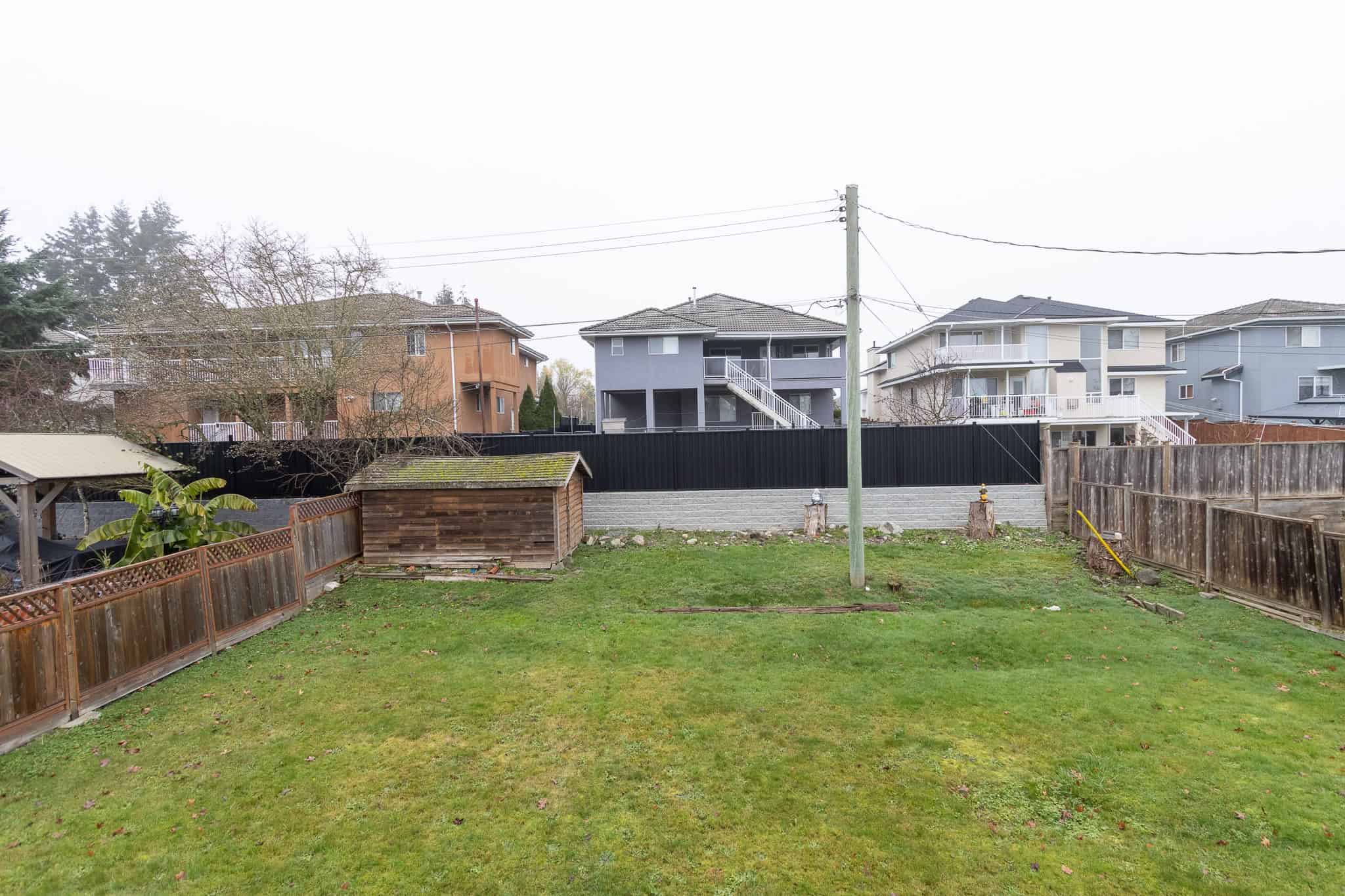 IMG_4367 Spacious backyard with green grass, wooden fence, storage shed, and neighboring multi-story homes, ideal for family living or outdoor activities in Vancouver.