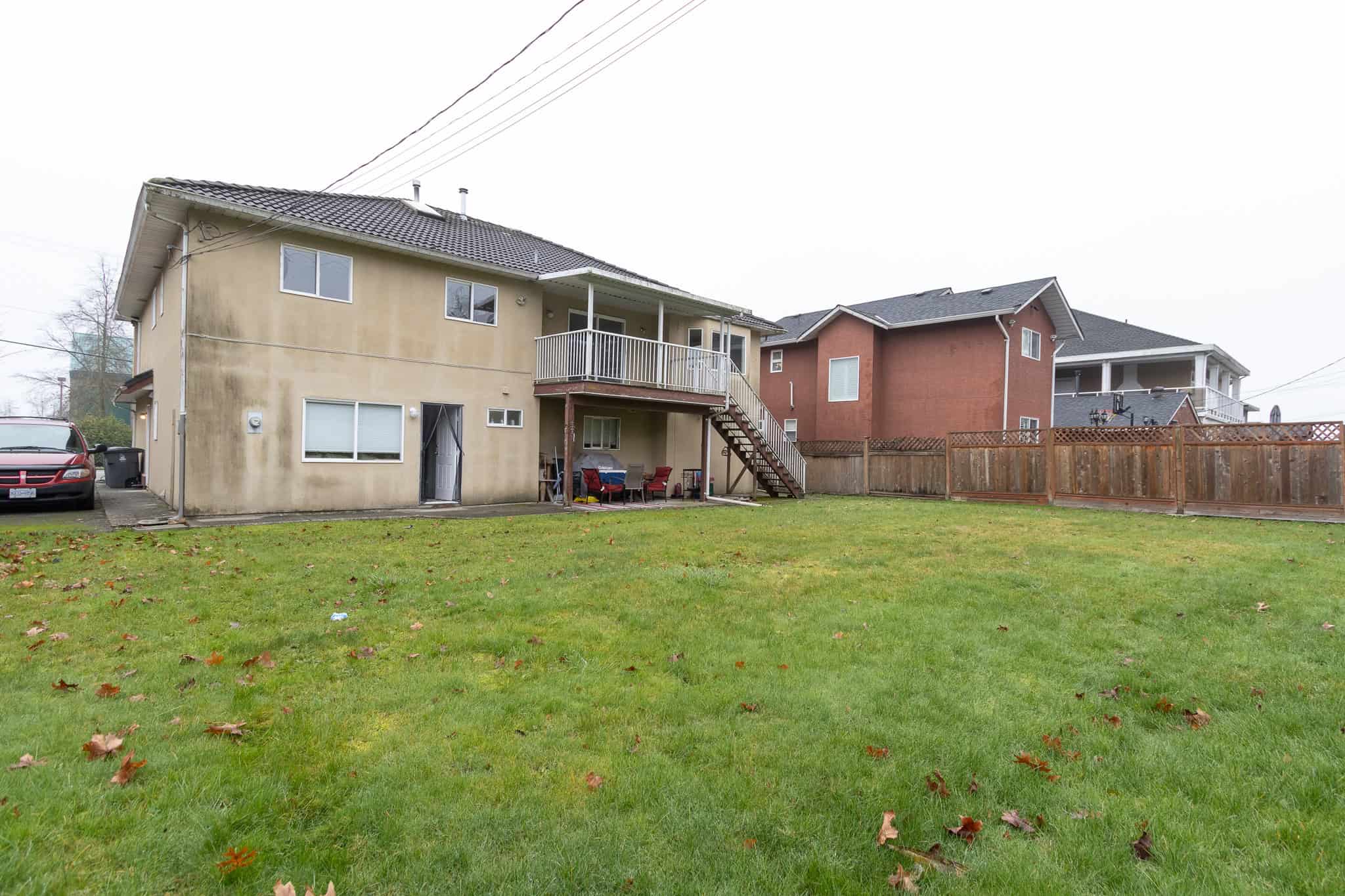 IMG_4380 Spacious backyard view of a multi-family home with a green lawn, outdoor seating area, and a wooden fence, showcasing Vancouver real estate opportunities with Orca Realty Inc.
