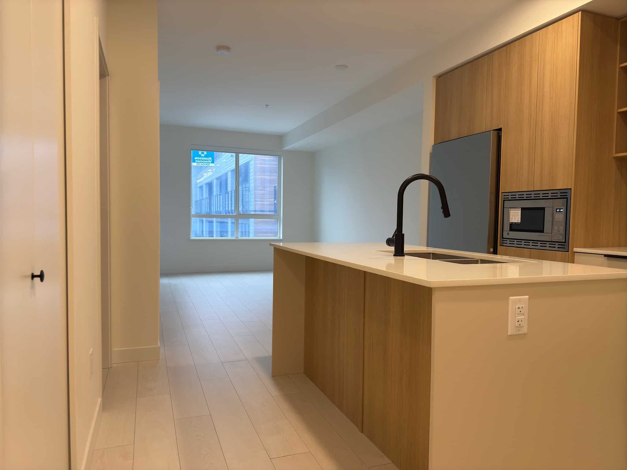 Modern open-concept kitchen with sleek cabinetry, black faucet, and built-in appliances in a contemporary downtown condo. Bright living space with large windows and light wood flooring.