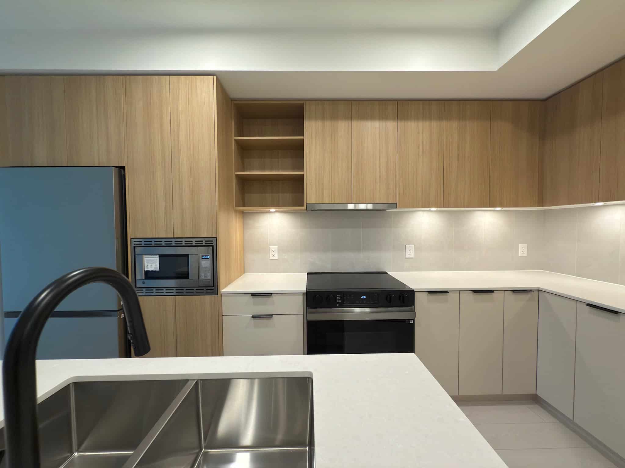 Modern kitchen with white countertops, light wood cabinetry, stainless steel appliances, and under-cabinet lighting, ideal for Vancouver real estate listings.