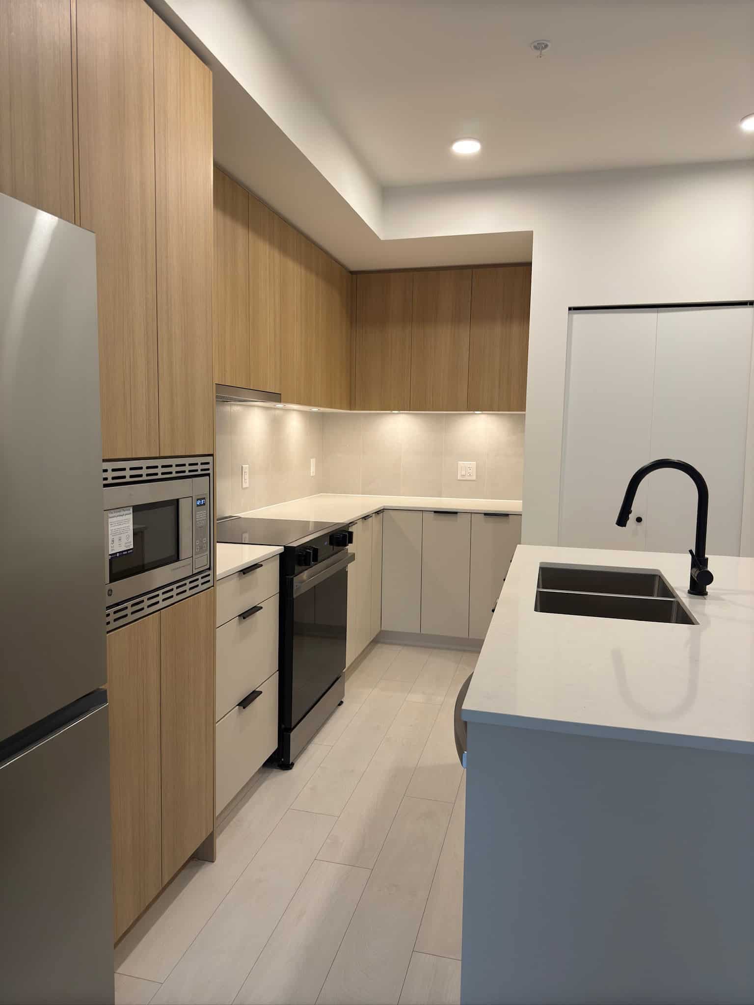 Contemporary modern kitchen with light wood and white cabinetry, stainless steel appliances, black fixtures, and minimalist design, perfect for Vancouver real estate and home renovation enthusiasts.