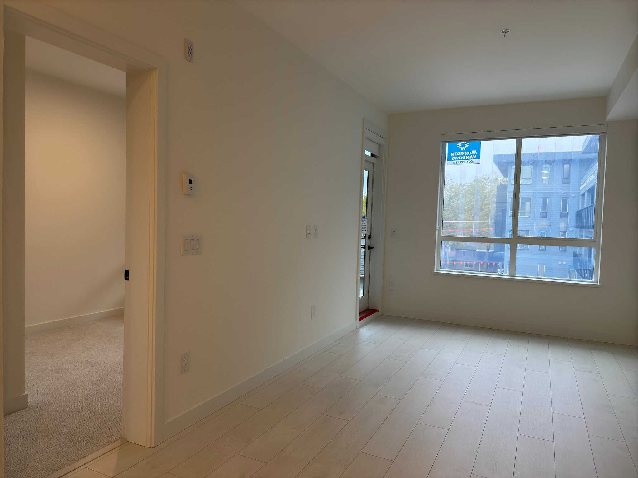 Bright modern living room with large window and sliding glass door, showcasing natural light and urban views in a new residential property listed by Orca Realty Inc.