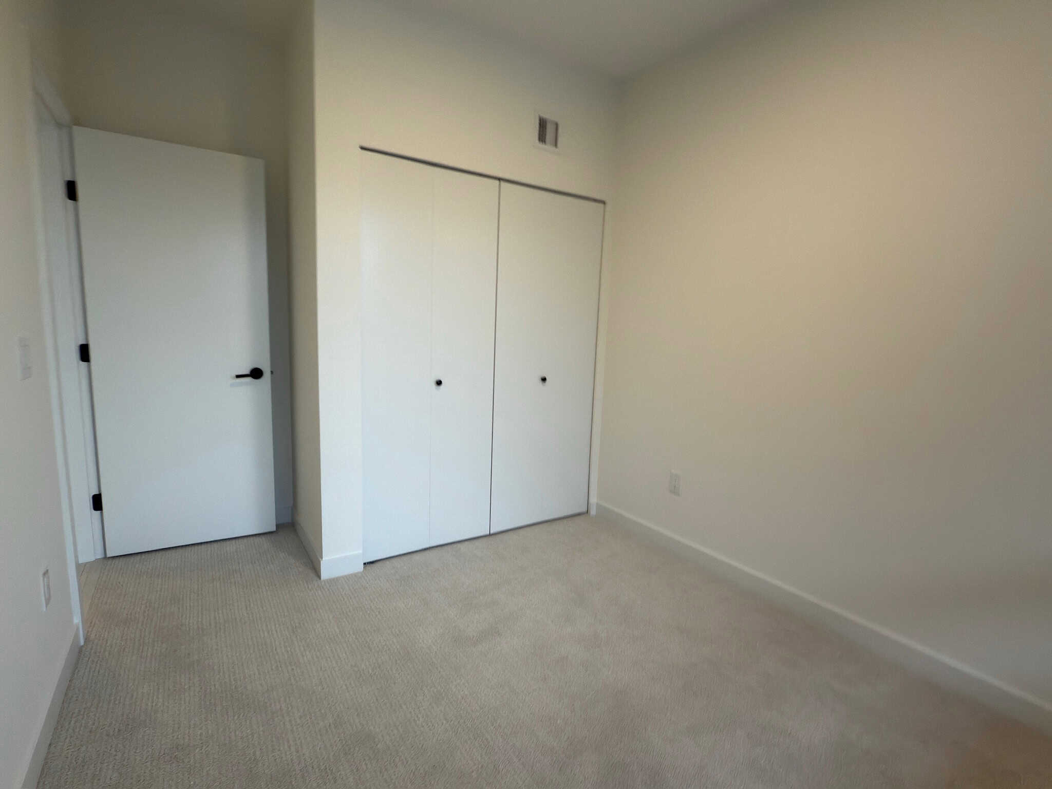 Bright, empty bedroom with white walls, beige carpet, and built-in closet, showcasing modern interior design.