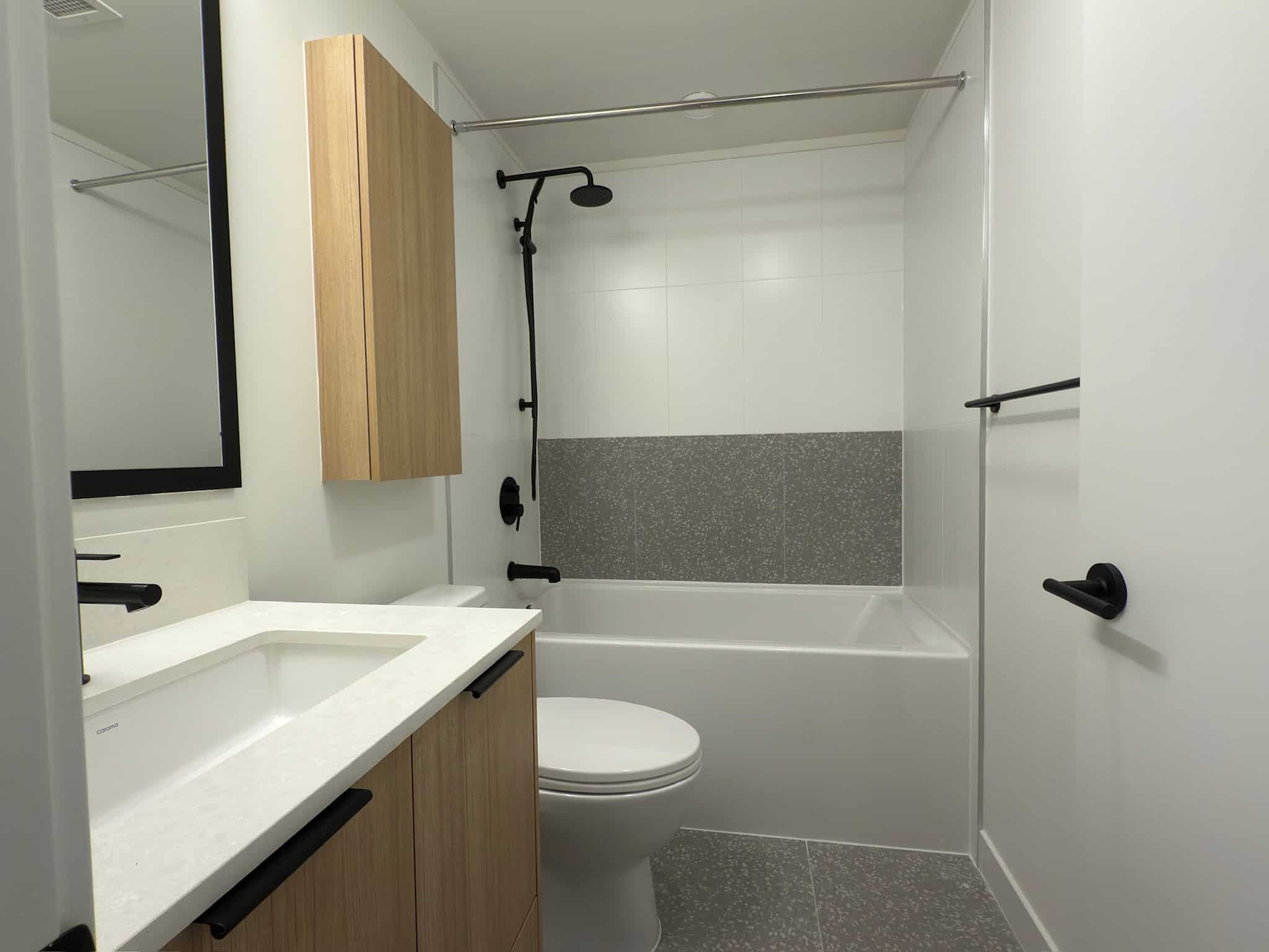 Modern bathroom with white walls, black fixtures, and wood accents, featuring a shower and vanity area, ideal for contemporary home living in Vancouver, BC.