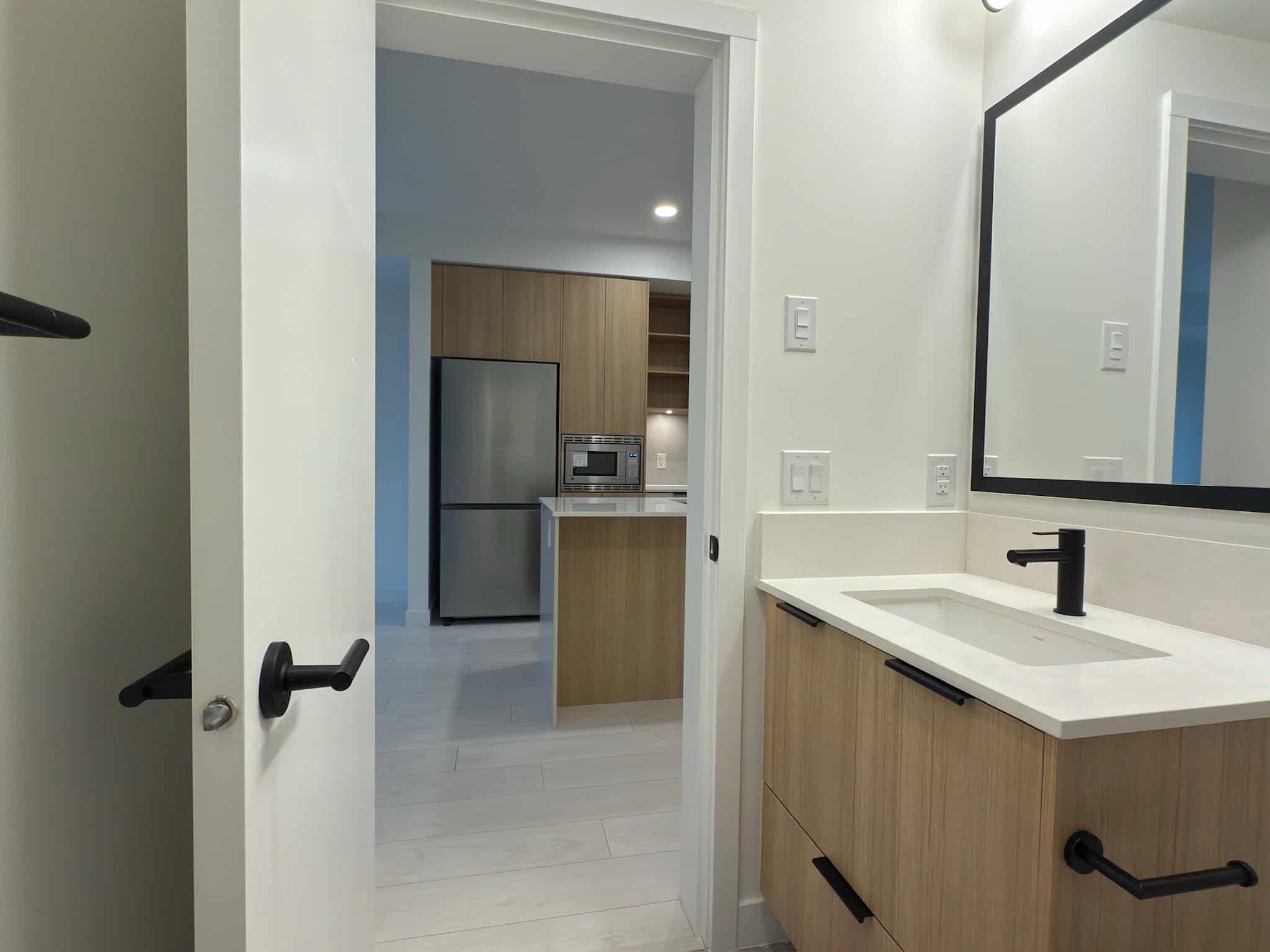 Modern bathroom with sleek wooden vanity, black fixtures, and large mirror, showcasing stylish and functional design elements ideal for Vancouver-area homes.