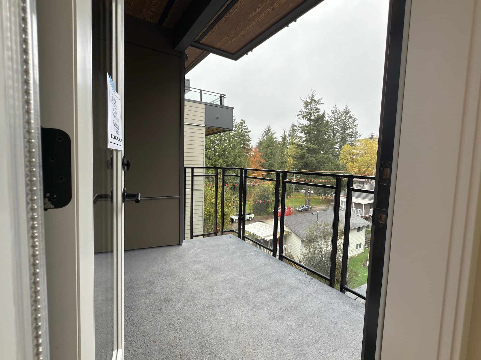 Bright balcony view from an apartment, overlooking trees and neighborhood streets, showcasing modern outdoor space.