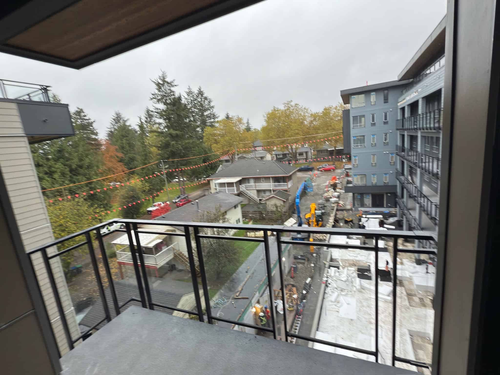 Construction site view from a balcony overlooking a residential area with adjacent buildings and trees, highlighting urban development and real estate opportunities.
