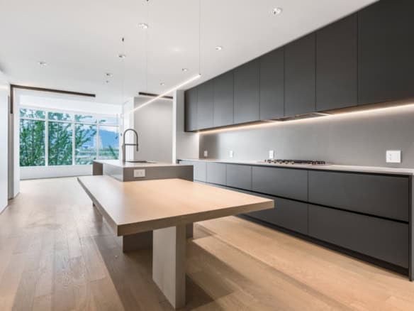Modern minimalist kitchen with sleek grey cabinetry, island with sink, and abundant natural light from large windows, highlighting contemporary home design and real estate opportunities by Orca Realty Inc.