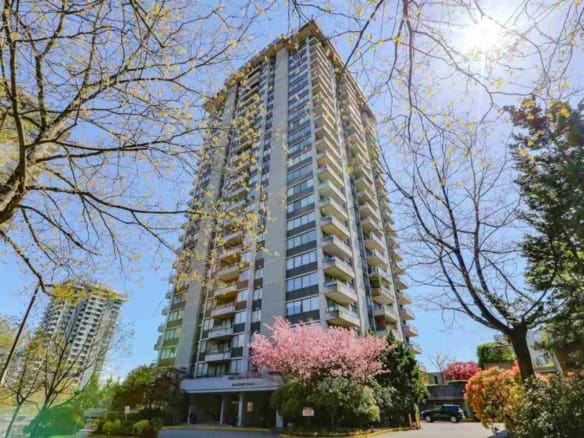 Modern high-rise apartment building with balconies, surrounded by blooming trees and lush greenery, located in a vibrant urban neighbourhood.