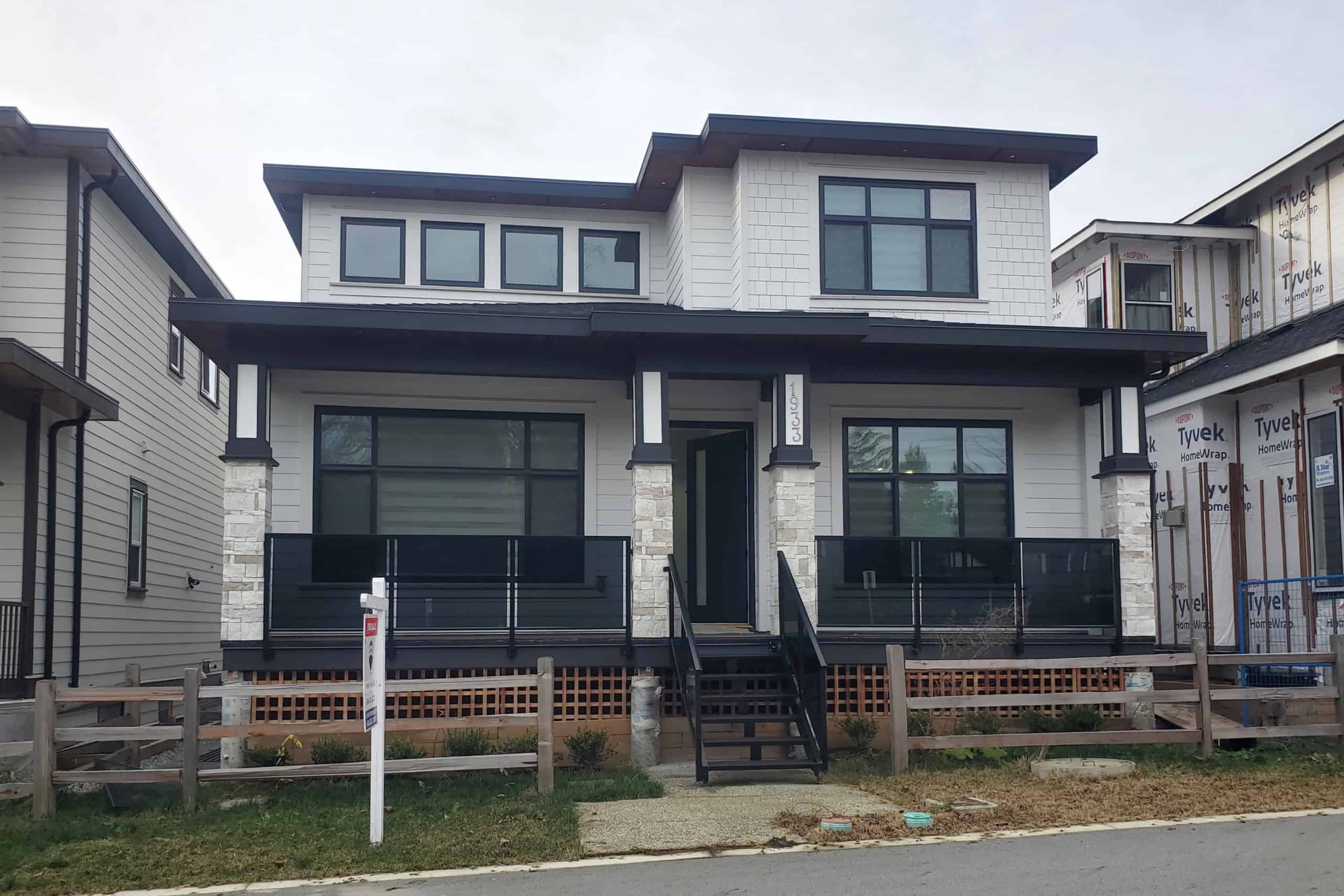 01 Modern newly built house with black and white exterior, multiple windows, front porch, and stone accents, in a residential neighbourhood, showcasing real estate opportunities by Orca Realty Inc.