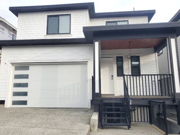 Modern new white house with black accents, front porch, and attached garage, showcasing contemporary architecture and curb appeal for Vancouver Island real estate.