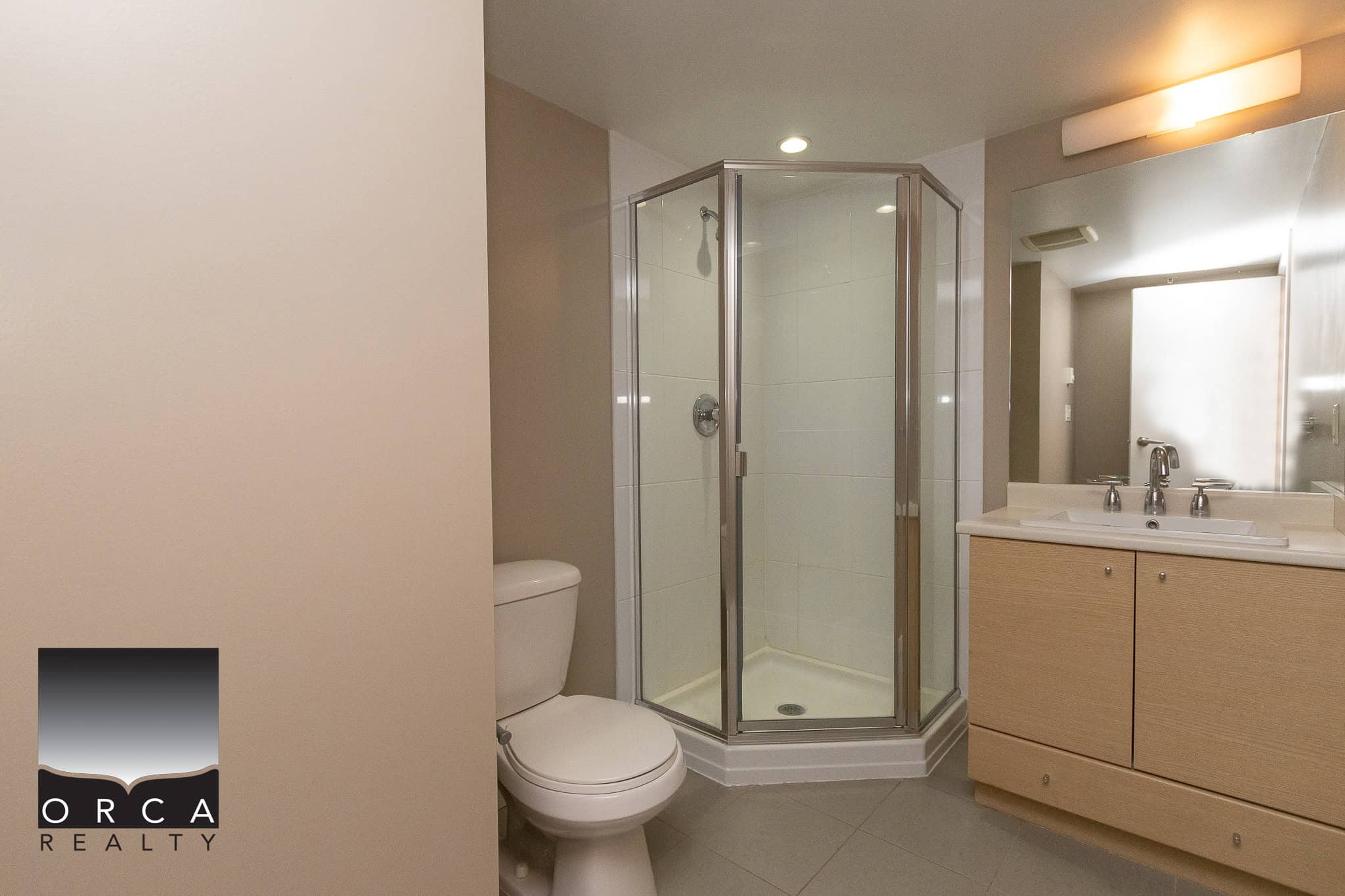 Modern beige bathroom with glass corner shower, white toilet, and wooden vanity with sink, in a contemporary residential property. Perfect for real estate listings in Vancouver or surrounding areas.
