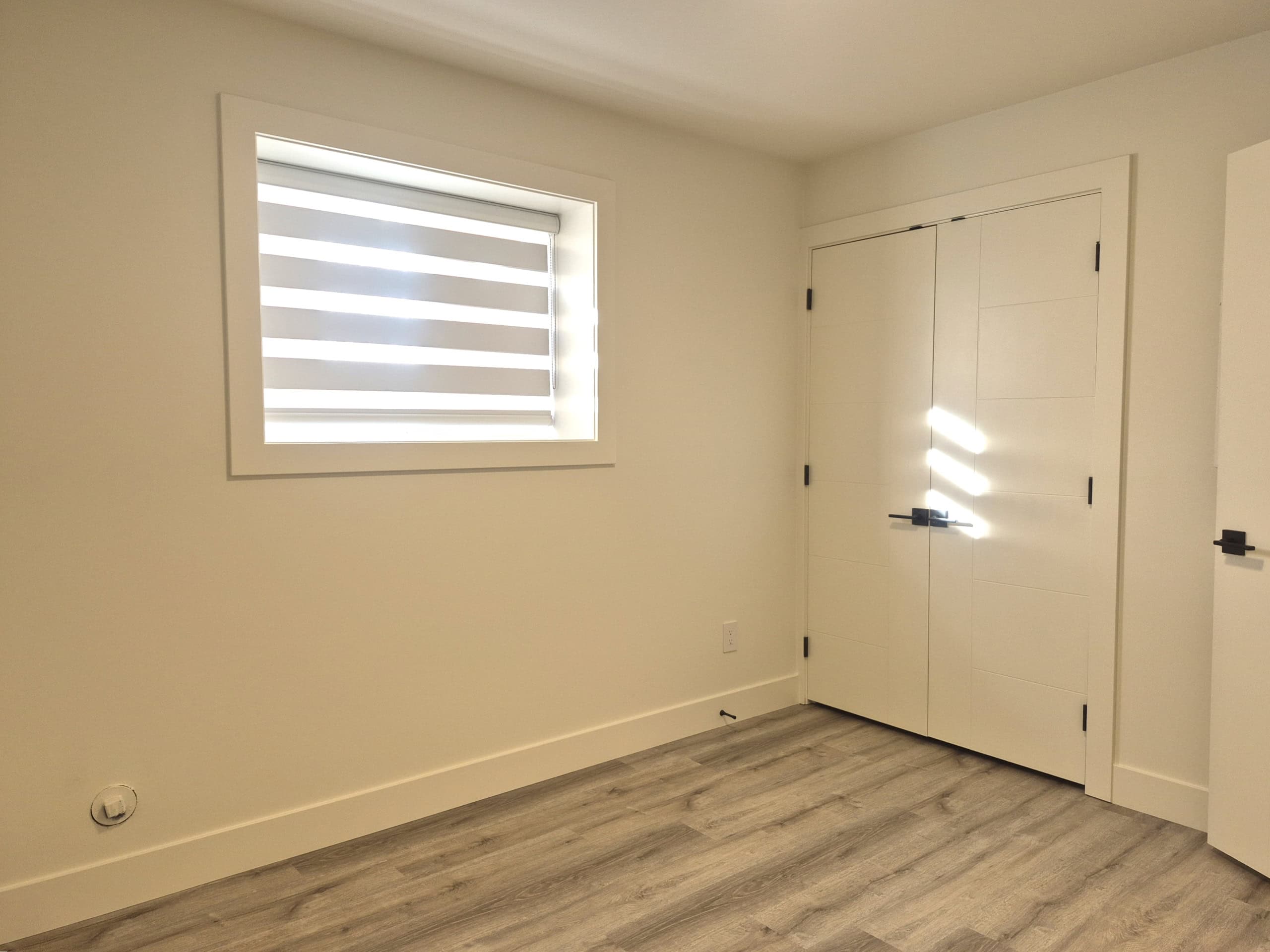 Modern interior room with white walls, a small window with zebra blinds, and light wood flooring, showcasing a minimalist design ideal for Vancouver real estate listings.