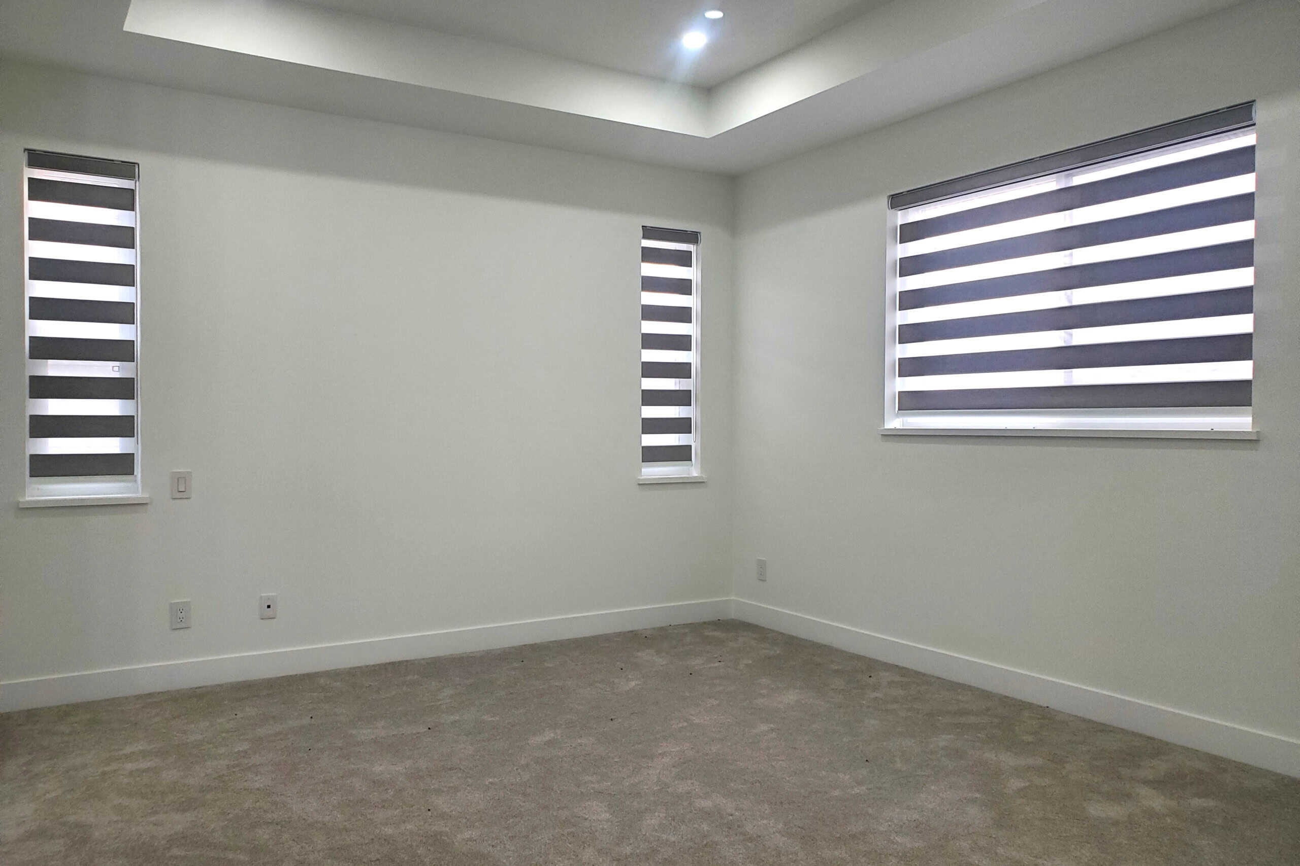12 Modern empty bedroom with three windows featuring black and white striped blinds, neutral wall paint, and beige carpet flooring, ideal for real estate listings or rental property showcase.