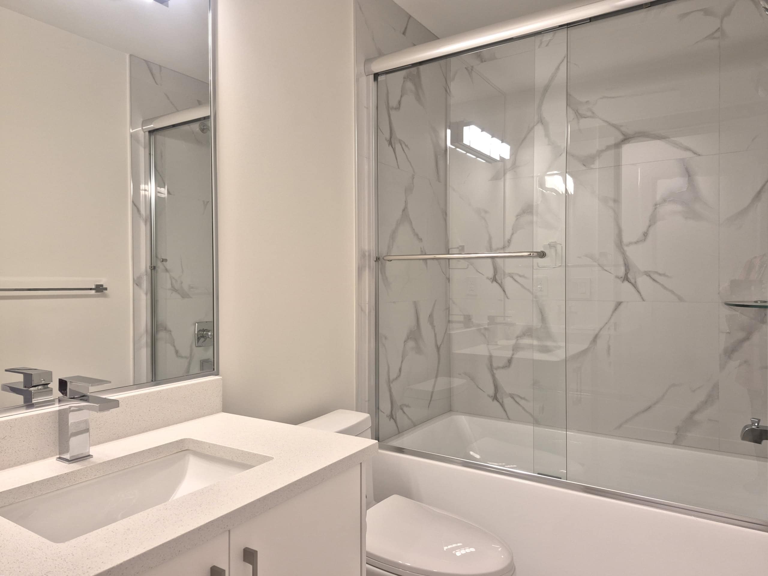 Modern bathroom with white vanity, sleek fixtures, and a shower/bathtub with marble-style tile surround – ideal for Vancouver Island real estate listings.