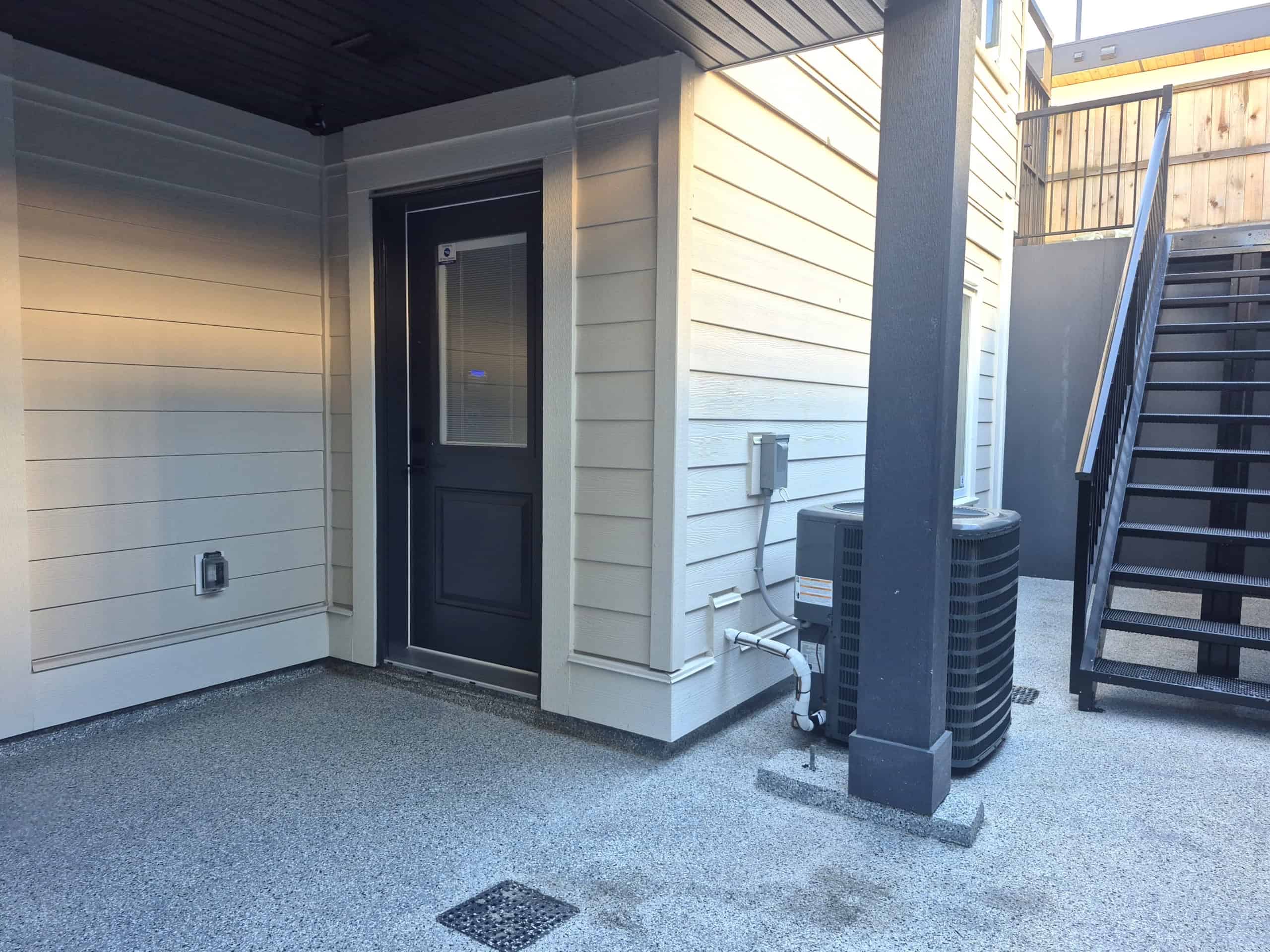 Modern townhouse exterior entrance with air conditioning unit and staircase, showcasing contemporary home features and outdoor space options.