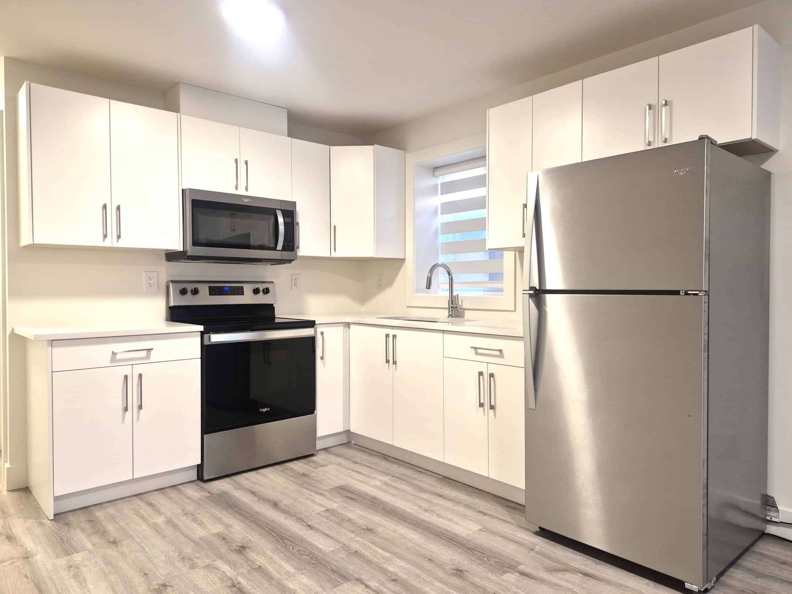 Modern white kitchen with stainless steel appliances including refrigerator, oven, microwave, and sleek cabinetry, perfect for Vancouver real estate listings.