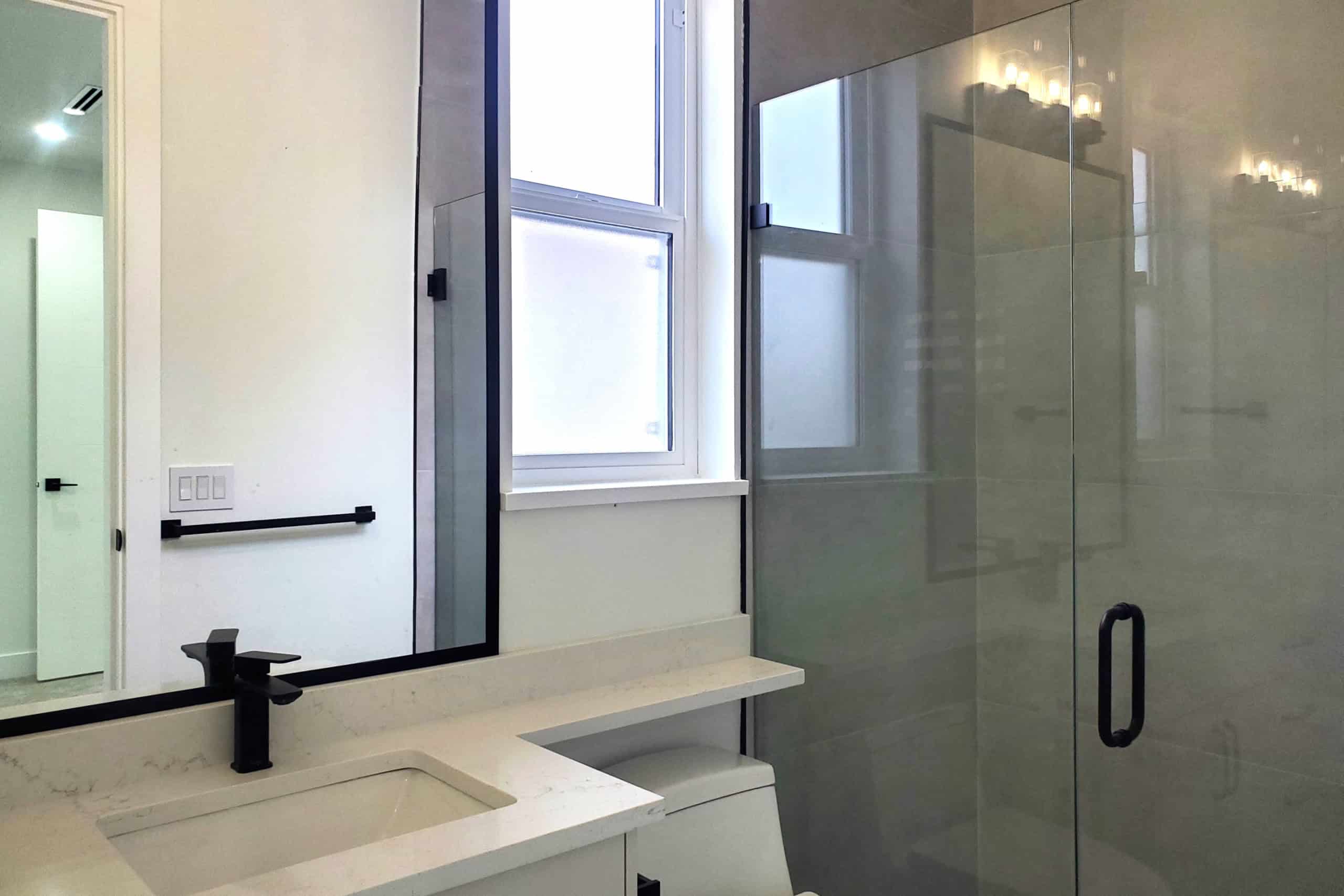 20 Contemporary bathroom interior with minimalist design, white vanity, black fixtures, frosted window, and glass shower enclosure, showcasing modern home features by Orca Realty Inc.