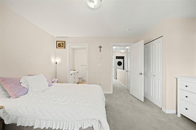 Bright and spacious bedroom in a modern home, featuring neutral decor, a large bed with white bedding, closet space, and easy access to an adjoining laundry area, ideal for families and couples.