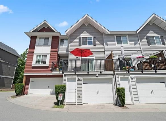 Modern multi-level townhouse with garages, outdoor balcony, and red patio umbrella, showcasing Vancouver Island’s vibrant real estate market in Mill Bay, BC.