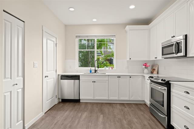 Modern white kitchen with stainless steel appliances, large window, and hardwood flooring, ideal for Vancouver island homes.