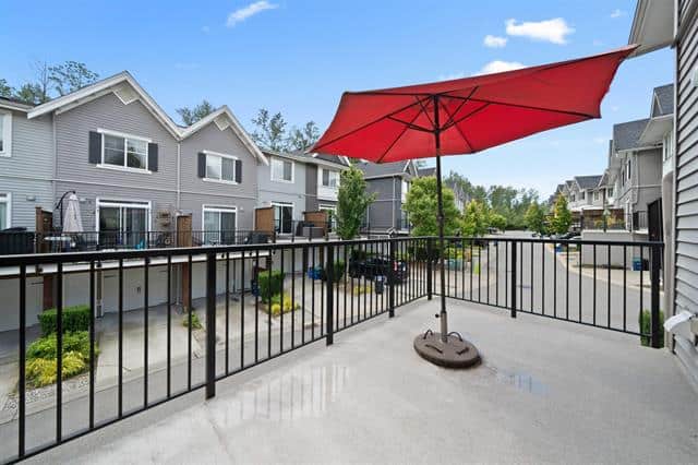 Spacious balcony with red patio umbrella overlooking a modern residential neighbourhood, ideal for relaxing or entertaining in Vancouver's suburban communities.