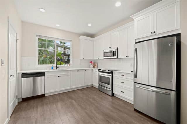 Spacious modern kitchen with stainless steel appliances, white cabinetry, large window, and hardwood flooring, ideal for Vancouver property listings.