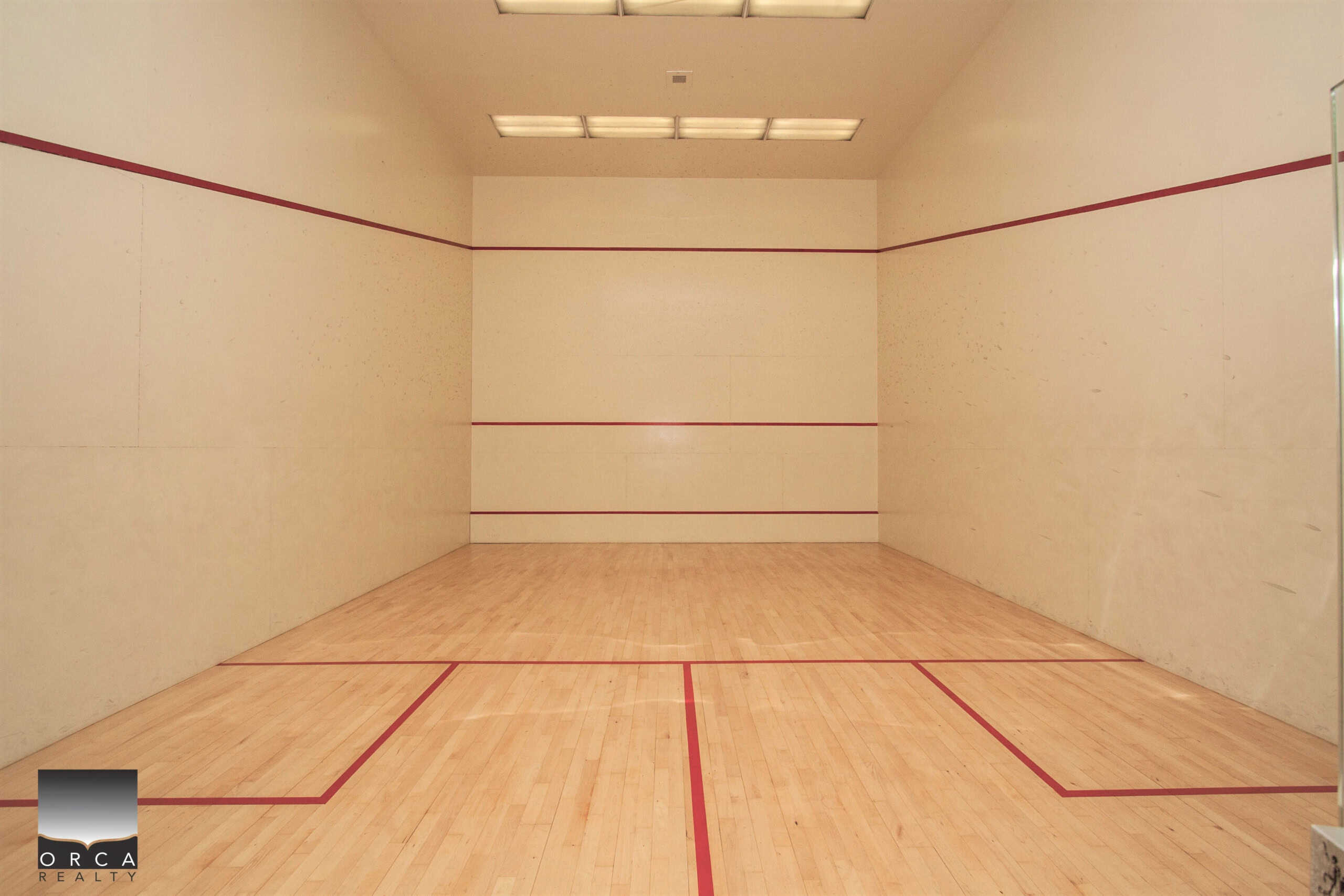 Bright indoor squash court with wood flooring and red boundary lines; ideal for fitness and sports enthusiasts.
