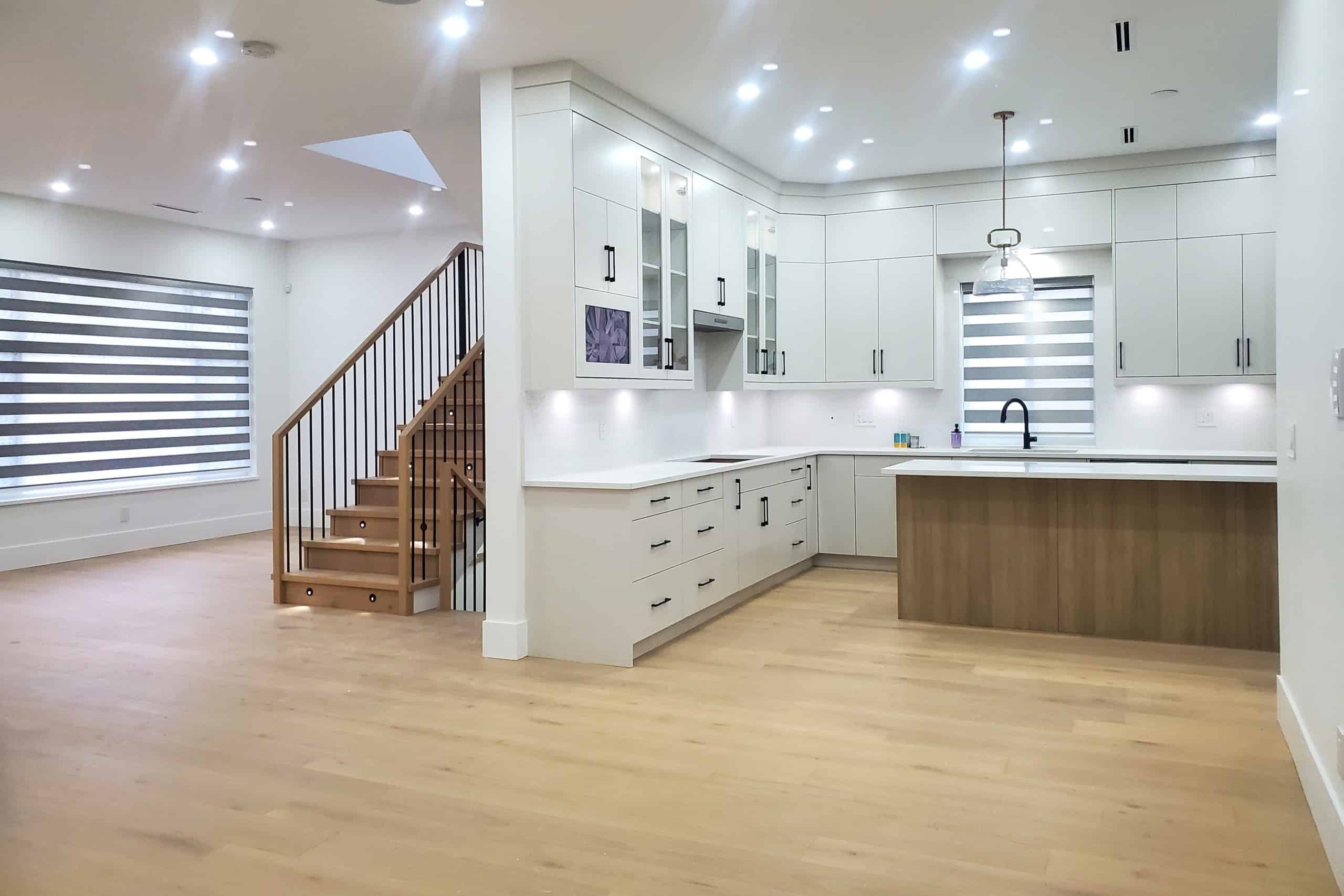 5 Spacious modern kitchen with white cabinets and black hardware, hardwood floors, and large window with striped blinds, showcasing contemporary interior design in a residential home.