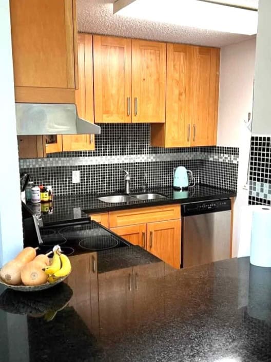 Modern kitchen with wooden cabinetry, black granite countertops, and black mosaic tile backsplash ideal for Vancouver real estate listings.