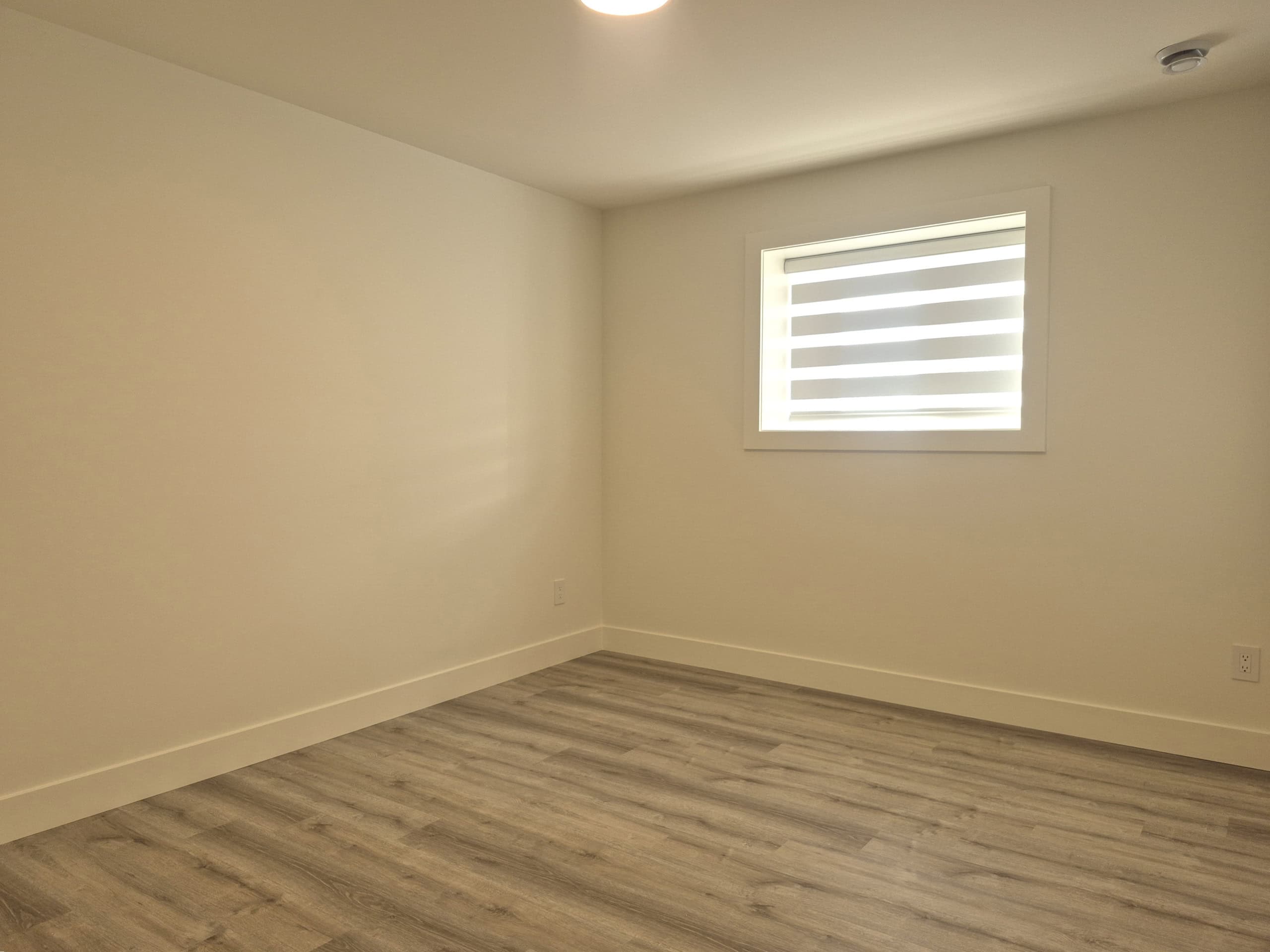 Bright empty room with large window and light wood flooring in a modern home, ideal for real estate purposes.