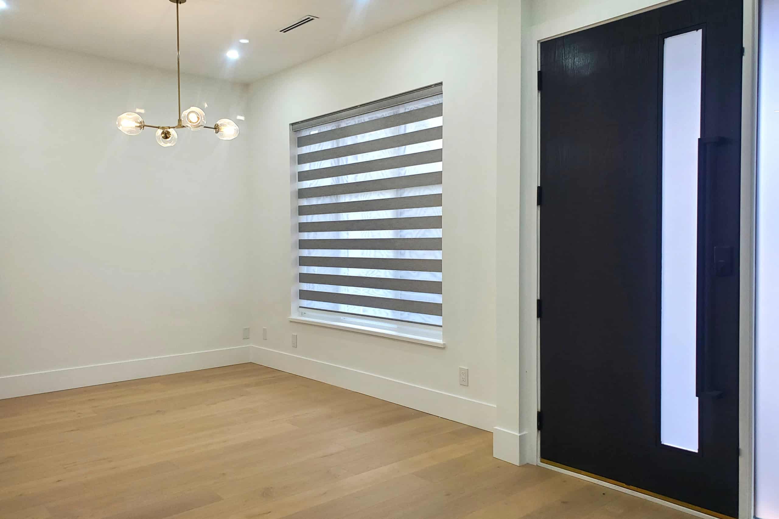8 Modern empty room with hardwood flooring, contemporary black front door, and stylish window with striped roller blinds, ideal for showcasing Vancouver Island real estate.