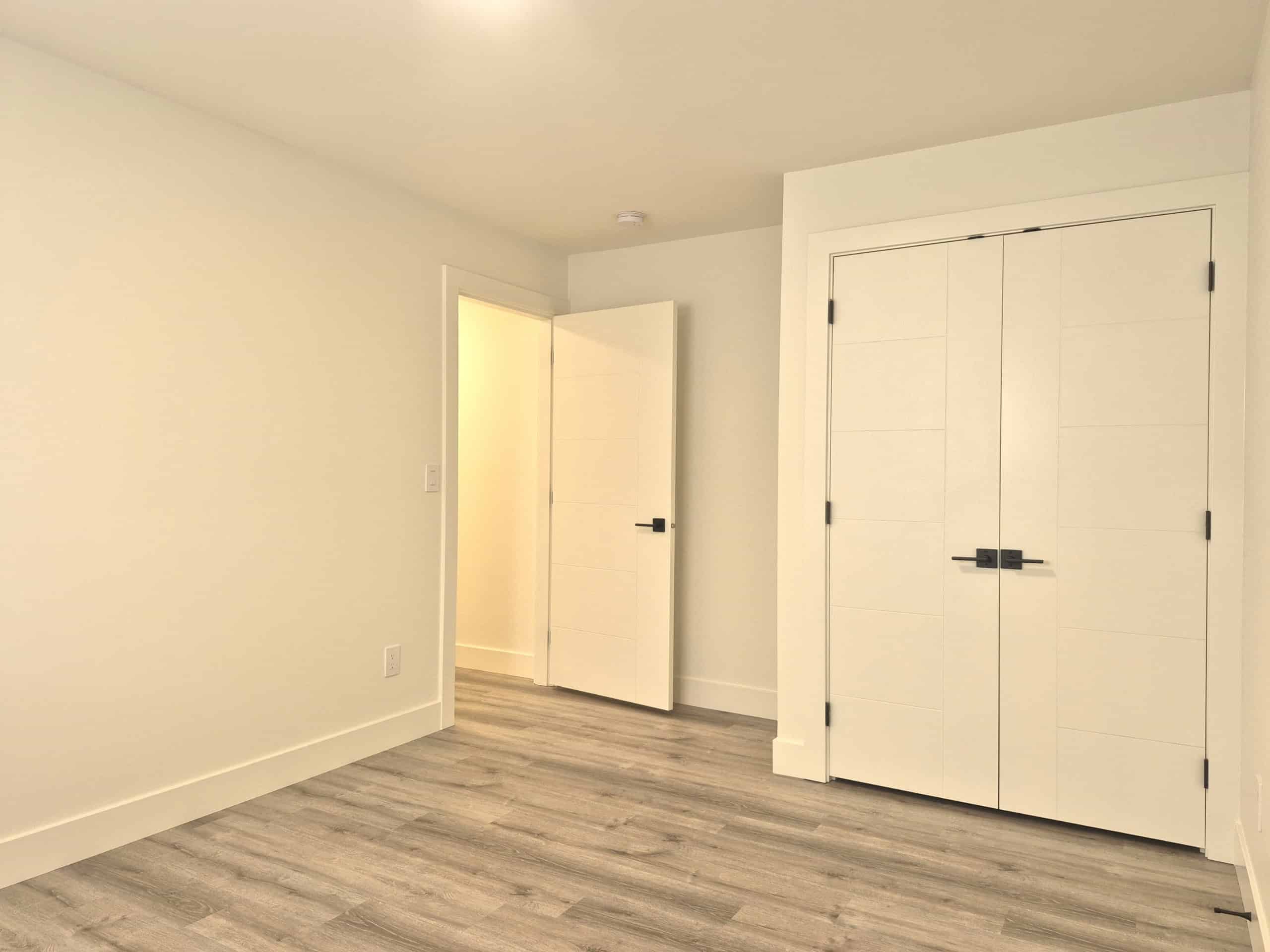Bright, modern bedroom with white walls, minimalist decor, and grey wood flooring, perfect for real estate listings showcasing contemporary Vancouver homes.