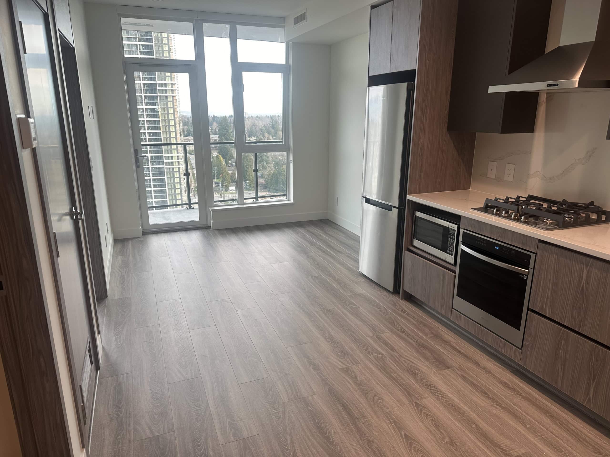 Modern high-rise apartment kitchen with stainless steel appliances and large balcony overlooking city skyline, ideal for urban living in Vancouver.