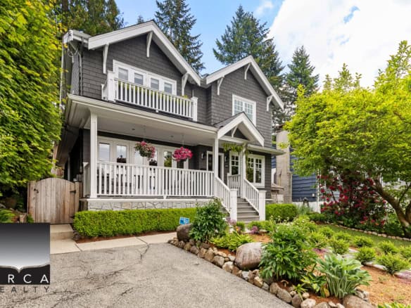 Charming grey Vancouver home with white accents, lush landscaping, and a welcoming front porch, showcasing beautiful garden beds and mature trees in a peaceful neighbourhood.