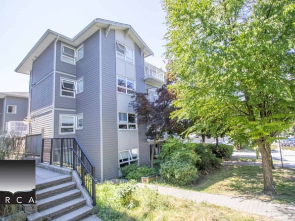 Modern multi-family residential apartment complex with grey siding, multiple windows, and a landscaped outdoor area in Victoria, BC, showcasing Orca Realty Inc. real estate services.