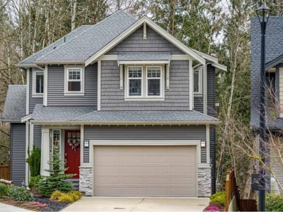 Modern grey two-storey house with stone accents and a red front door, located in a lush suburban neighbourhood in British Columbia, perfect for families and real estate investment.