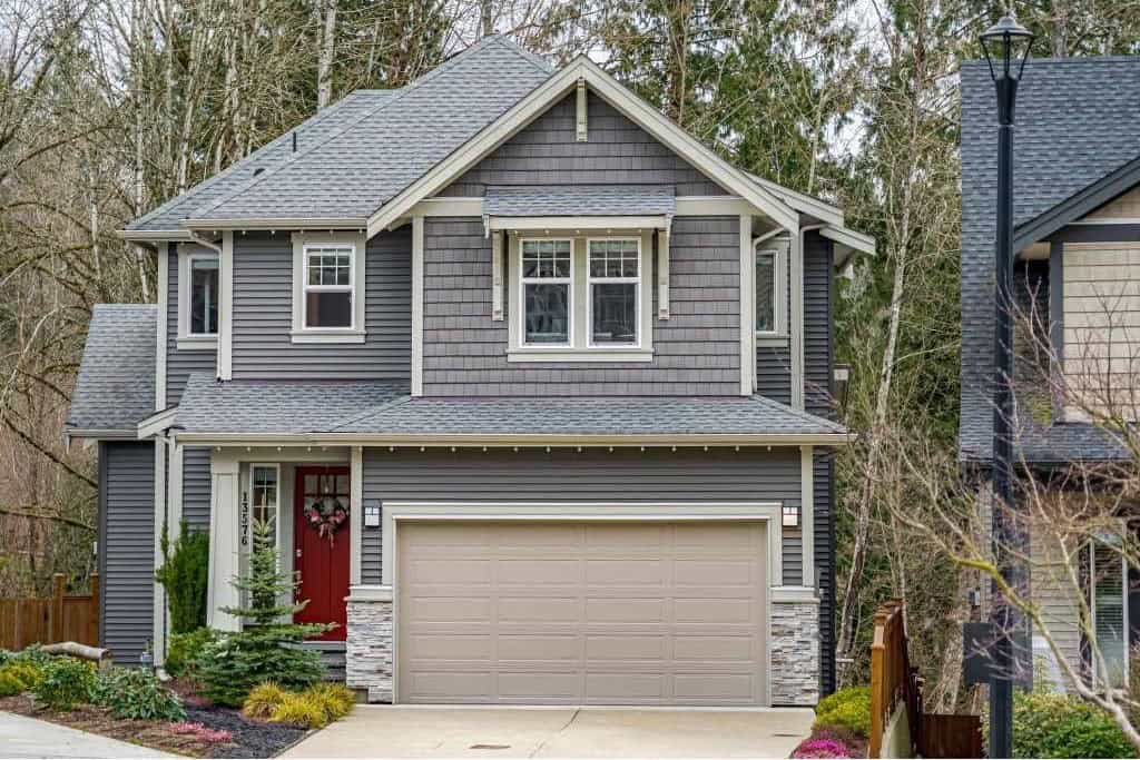 Modern grey two-storey house with stone accents and a red front door, located in a lush suburban neighbourhood in British Columbia, perfect for families and real estate investment.