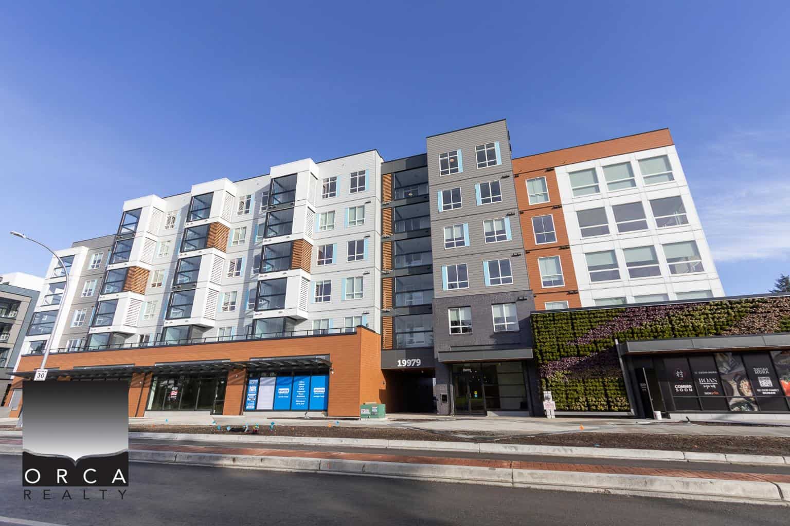 Contemporary multi-family residential building with modern architecture, large windows, and commercial ground-floor units, located in a vibrant urban area in Vancouver, BC.