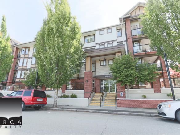 Bright multi-story residential apartment building with modern architecture, red brick accents, and large windows, surrounded by lush green trees and parked cars, located at 5660, in a vibrant neighbourhood.